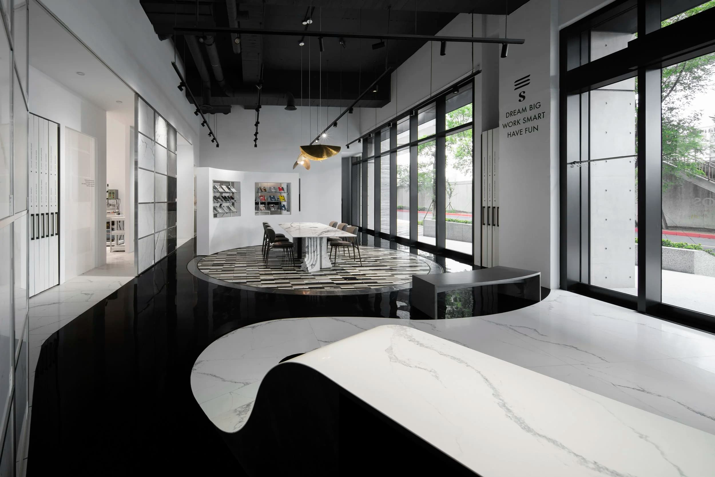 Modern interior of a building with white and black design elements, large windows, a marble table, chairs, and decorative lighting.